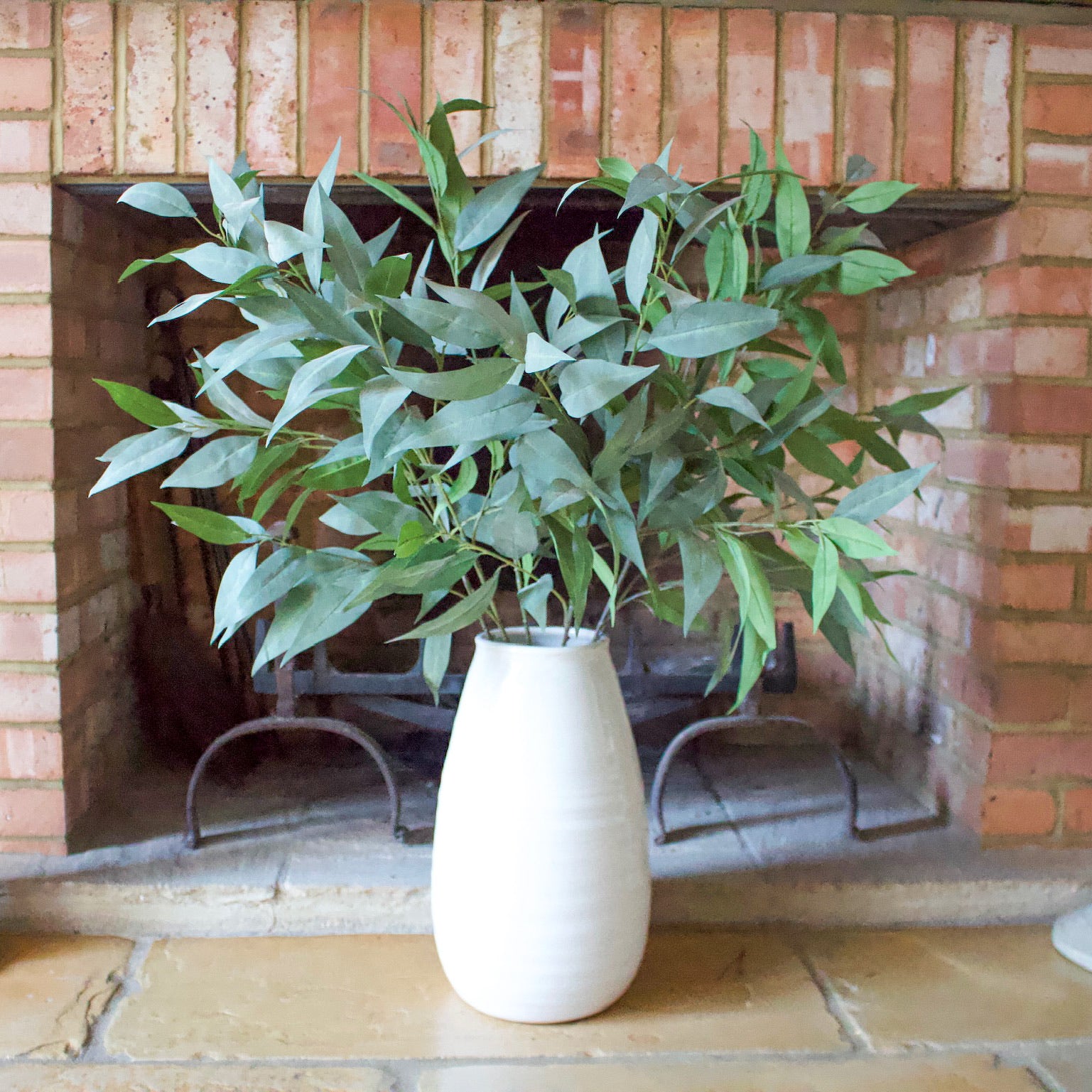artificial green eucalyptus stems in white vase